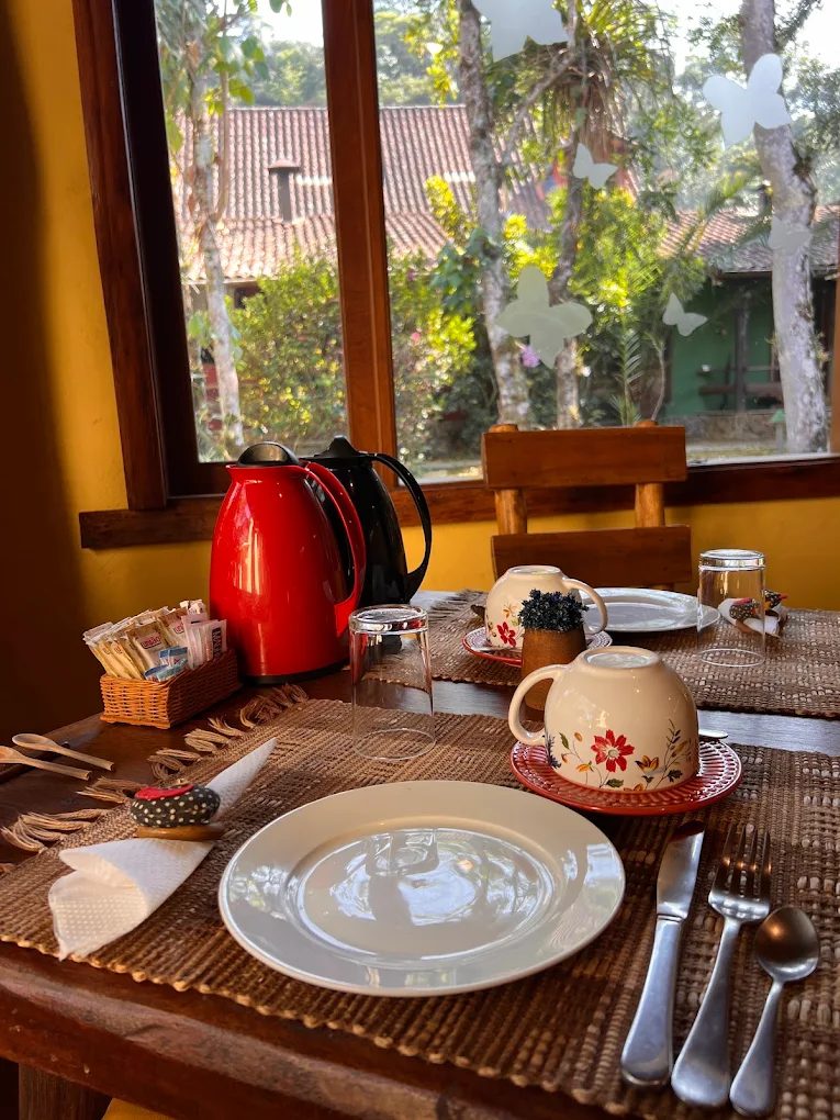 Mesa de café posta ao lado da janela, com garrafas térmicas e xícaras floridas